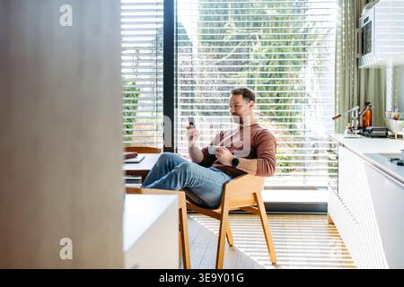 Man controlling smart home system and adjusting exterior blinds using phone at home. Stock Photo