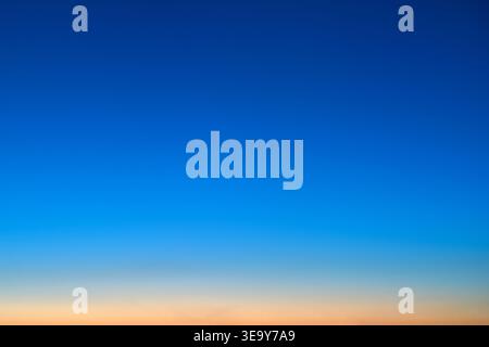Clear blue sky with a soft orange gradient on the horizon at sunset. Abstract natural background with copy space. Evening light transition in the atmo Stock Photo
