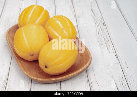 Fresh Korean yellow melons in a wooden bowl on a white vintage wood background. Stock Photo