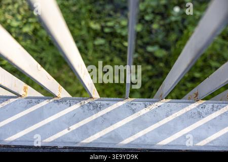 Abstract top view perspective showing bright sunlight casting diagonal line shadow from metal fence railing onto concrete ledge with soft blurred gree Stock Photo