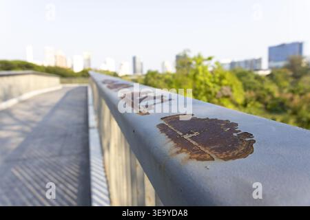 Close up view showing rusty metal railing on pedestrian bridge walkway overlooking blurred urban park skyline revealing calm peaceful nostalgic feelin Stock Photo