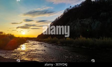 Quiet evening scene on a calm river bordered by glowing shrubs. Cool blue light and gentle ripples carry the day into night across the valley. Stock Photo