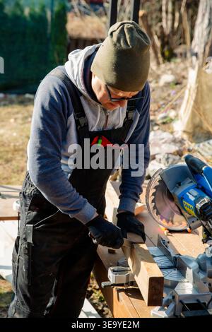 Professional carpenter using miter saw cutting wood outdoors for home improvement, construction and sustainable DIY in backyard. Stock Photo