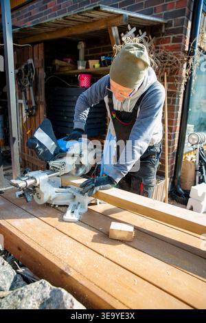 Professional carpenter using miter saw cutting wood outdoors for home improvement, construction and sustainable DIY in backyard. Stock Photo