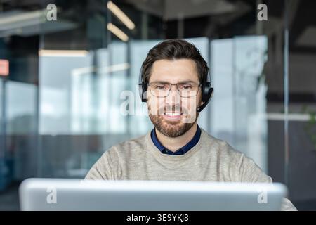 Friendly male customer service representative working in an office, wearing a headset and glasses, providing professional assistance and online technical help Stock Photo