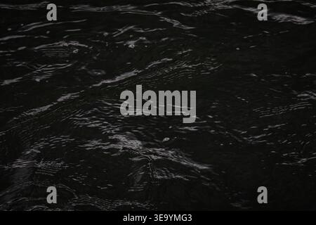 Dark ripples spread across water forming delicate lines and soft highlights. An abstract surface shifts with quiet motion creating a moody background Stock Photo