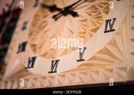 Macro view of an ornate wooden clock shows bold roman numerals rising from a carved geometric dial. Warm timber tones and shallow focus celebrate hand Stock Photo