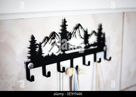 Metal wall rack with a silhouette of mountains and pine trees offers multiple hooks for keys towels or leashes on a tiled wall. Stock Photo