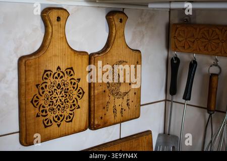 Pair of wooden cutting boards hangs as kitchen art. Pyrography patterns include a detailed mandala and a dreamy moon motif. Warm tones and visible Stock Photo