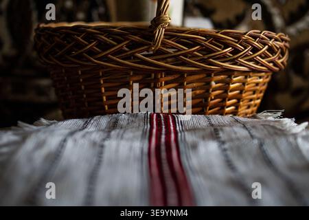 Wicker basket sits above a fringed handwoven cloth featuring a bold red stripe. Warm tones and soft shadows create a cozy rustic atmosphere Stock Photo