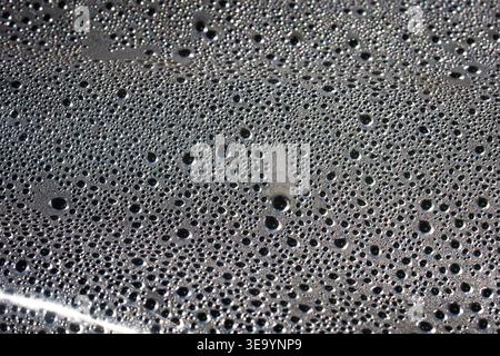 Tight macro of water beads across a metallic surface. Perfect spheres sparkle under sun as surface tension shapes a patterned field that reads like Stock Photo