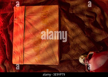 Old leather notebook on vibrant fabric background. Ancient leatherbound journal with shadowy ambiance and occult elements Stock Photo