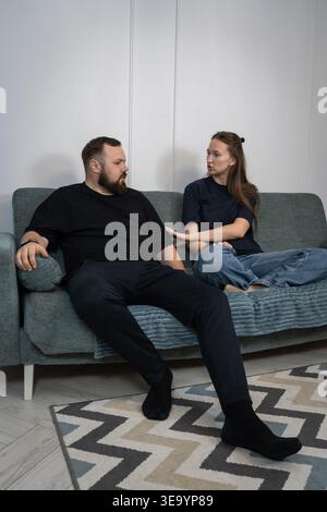 Young couple lounging on a sofa at home, laughing and chatting comfortably, sharing a relaxed intimate moment that captures everyday connection and do Stock Photo