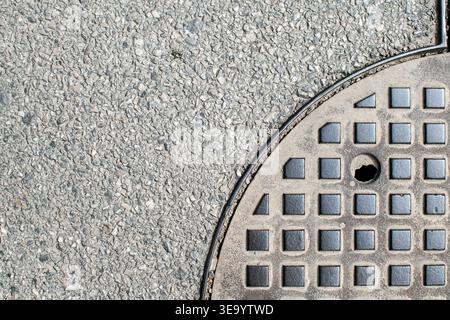 Partial round manhole cover with textured asphalt creating urban industrial copy space background. Stock Photo