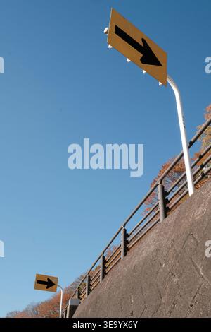 Two yellow arrow signs pointing right against a clear blue sky with autumn trees Stock Photo