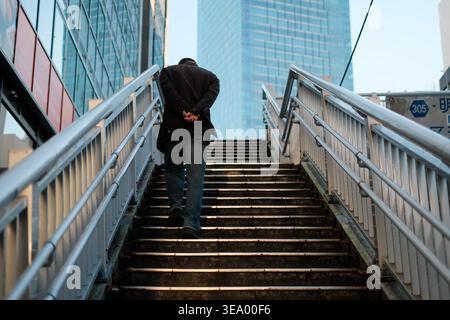 Man climbing city stairs with hands clasped behind back Stock Photo