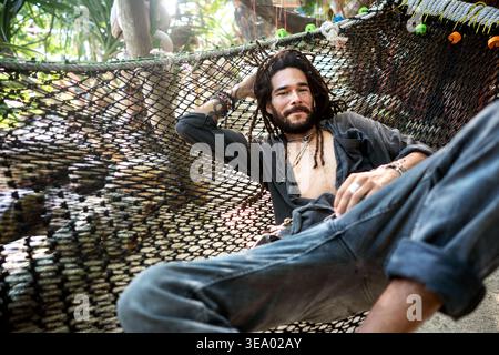 handsome fashion guy with dreadlocks on the beach lies on a hamm Stock Photo