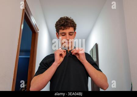 Young man wearing a black polo shirt, buttoning up his collar, getting ready for the day or an important occasion Stock Photo