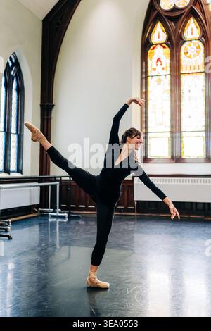 Ballerina performing arabesque in dance studio with stained glass Stock Photo