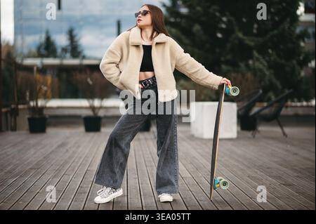 Woman in street clothes posing with skateboard in hands Stock Photo