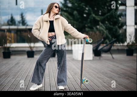 Woman in street clothes posing with skateboard in hands Stock Photo