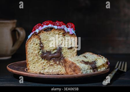 Close up of sliced traditional festive cake with chocolate filling topped with icing sprinkles and red cherries on dark rustic background. Gourmet chr Stock Photo