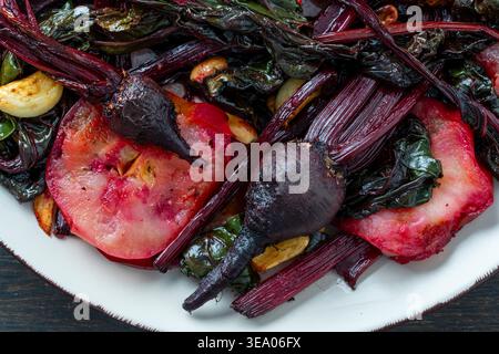 Roasted baby beets with apples and garlic greens, close up. Gourmet roasted baby beets served with sliced apples, garlic, and sauteed beet greens. Hea Stock Photo