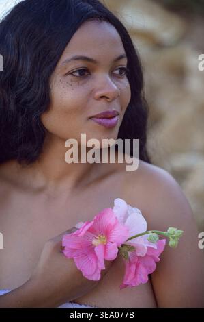 Profile portrait of a young Black woman holding pink mallow flowers Stock Photo