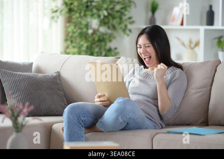 Excited asian woman checking paper documents sitting on a couch at home Stock Photo