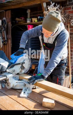 Professional carpenter using miter saw cutting wood outdoors for home improvement, construction and sustainable DIY in backyard. Stock Photo