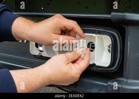 Close up of hands installing a new glass bulb into the tail light socket of a vehicle. Automotive electrical maintenance. Stock Photo