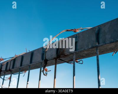 rusty old barbed wire on fence against blue sky Stock Photo
