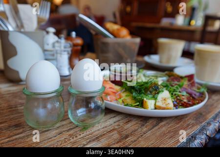 Soft boiled eggs in glass cups served with a gourmet breakfast platter featuring smoked salmon, cheeses, microgreens, and hot coffee in a cozy restaur Stock Photo