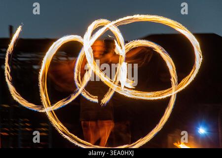 Dynamic rear view of a male fire dancer performing with spinning flames at an outdoor night show in Dubai, UAE. Stock Photo
