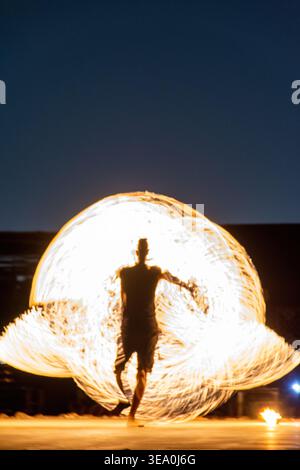 Dynamic rear view of a male fire dancer performing with spinning flames at an outdoor night show in Dubai, UAE. Stock Photo