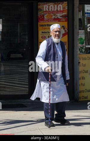 An older Muslim man wearing a Kufi hat & kurta shirt walking with a cane on 37th Ave in Jackson Heights, Queens, New York City. Stock Photo