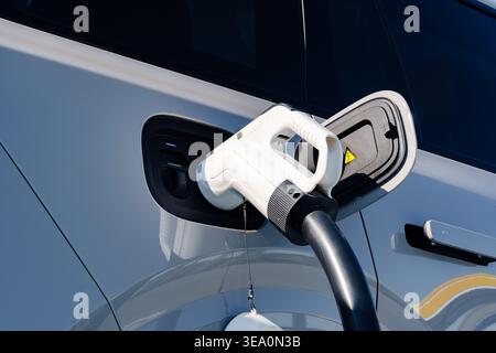 Electric car charger connected to vehicle at a charging station in the daytime Stock Photo