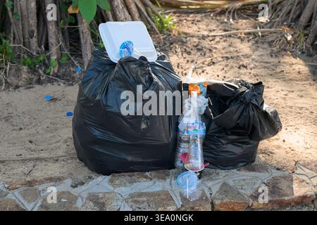 A stark, high-contrast photograph depicts the reality of environmental impact in a tourist destination, showing two large black plastic garbage bags a Stock Photo