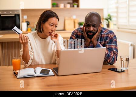 Multiracial couple is shopping online at home. They are using laptop and credit card. Stock Photo