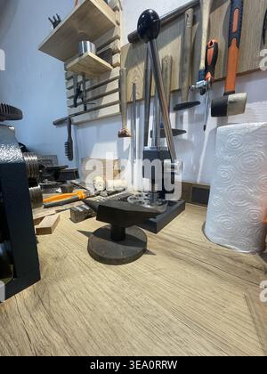 A manual press sits on a wooden table in a workshop filled with tools. Surrounding it are materials and various hand tools, indicating active crafting Stock Photo