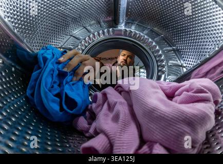 Man Loading Colorful Clothes into Washing Machine Drum, Inside View Stock Photo