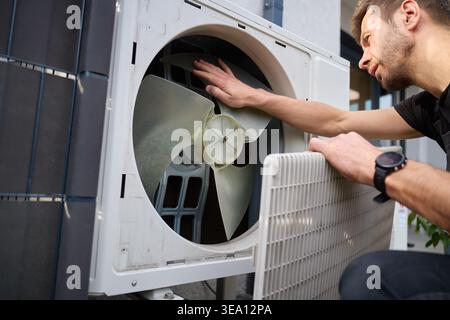 Technician removing front cover and inspecting fan inside outdoor heat pump unit. Concept of HVAC maintenance, repair service and energy efficient hom Stock Photo