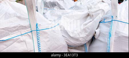Close up of white woven construction sacks packed with materials waste and secured with blue straps. Stock Photo