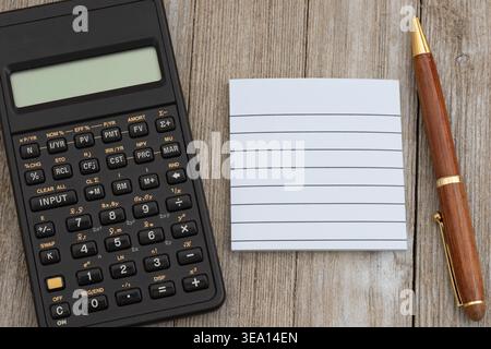 Black calculator with lined note pad and wood pen on rustic brown desk, ideal for budgeting, planning, accounting, and finance themes Stock Photo