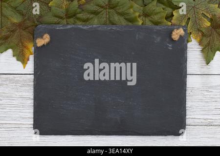 Empty slate board sign with autumn oak leaves on white wooden background, ideal for menu display, seasonal messages, or school messages. Stock Photo