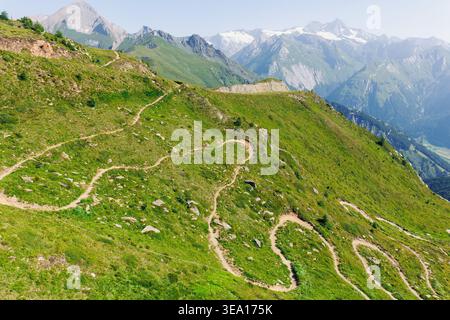Scenic aerial panoramic view curvy winding serpentine dirt path road alpine mountain peak with green wild grassland meadow and rocky horizon sky Stock Photo