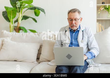Senior man doctor working with laptop computer. Professional senior mature healthcare expert searching information or have online consultation in hospital room. Medicine healthcare medical checkup Stock Photo