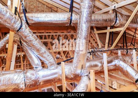 Workers are installing metal ductwork in attic of construction site, wooden beams support structure. Stock Photo