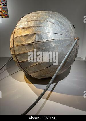 Metallic spherical object with segmented panels. It rests on a polished floor surface. Cable extends from its side toward the foreground. Soft lightin Stock Photo