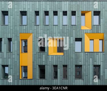 Modern facade with green cladding and yellow window accents. A contemporary building exterior featuring green vertical panels and recessed windows. Stock Photo